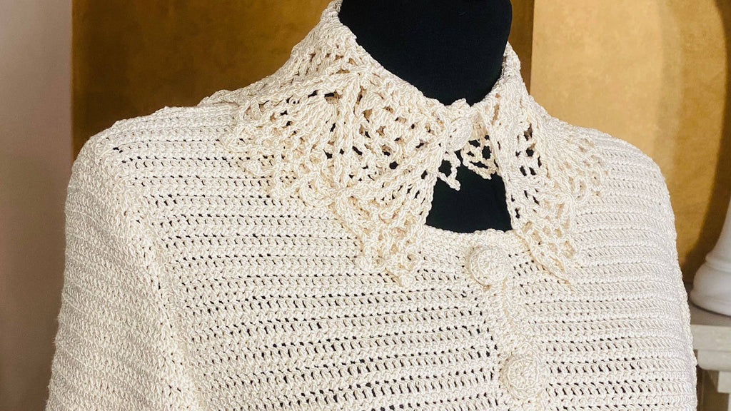 An off-white crocheted cardigan sweater with a large, ornate lace-like collar, displayed on a black mannequin torso.