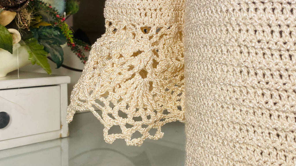 Close-up of a cream-colored crocheted textile, likely a chair or sofa armrest, showing detailed lace and openwork crochet patterns.
