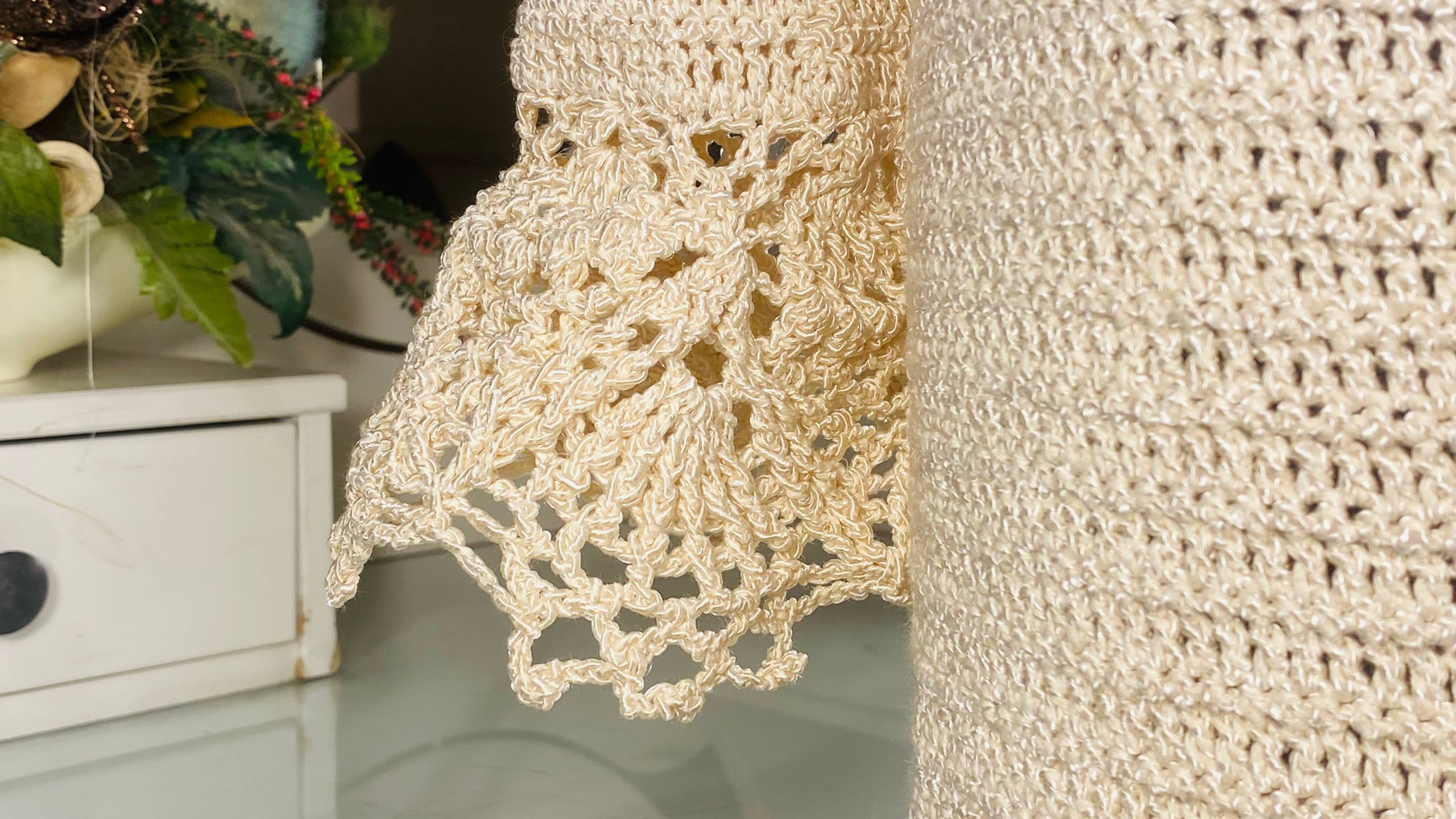 Close-up of a cream-colored crocheted textile, likely a chair or sofa armrest, showing detailed lace and openwork crochet patterns.