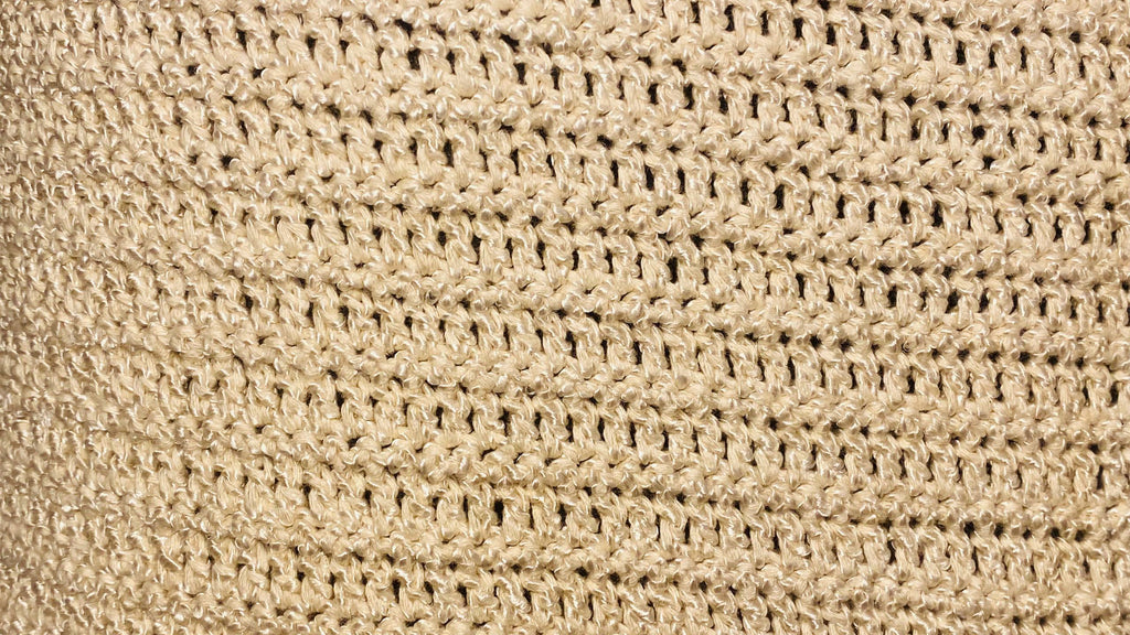 Close-up of a beige woven or crocheted textured material with a repeating open-stitch pattern.