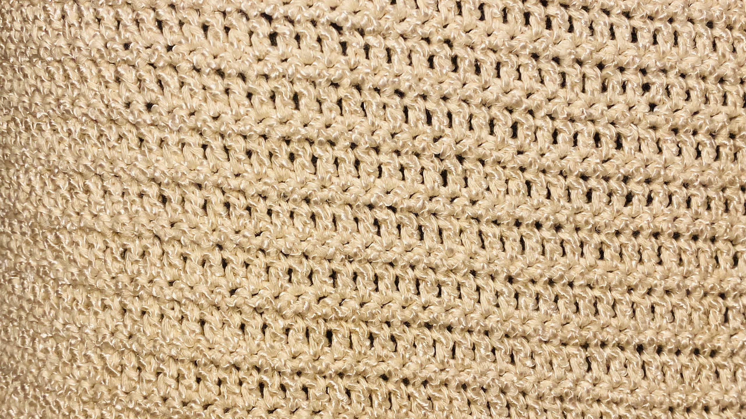 Close-up of a beige woven or crocheted textured material with a repeating open-stitch pattern.