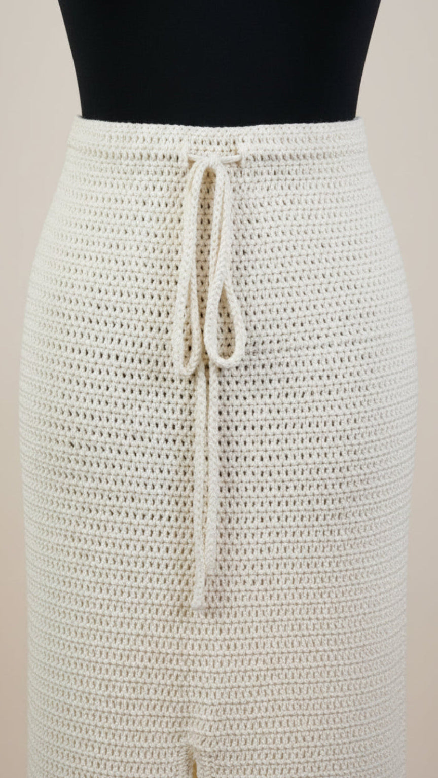 An off-white crochet knit skirt with a drawstring waist, displayed on a black mannequin torso against a light beige background.