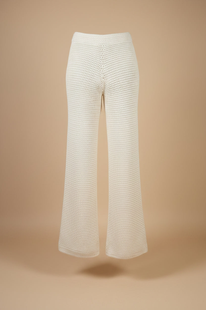 White crochet knit wide-leg pants displayed on a black dress form mannequin, set against a beige wall and wooden floor.