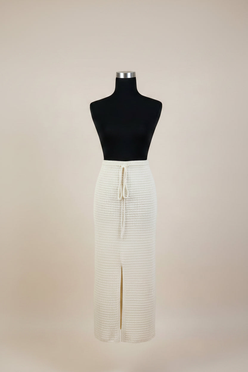 An off-white ribbed knit midi skirt with a front slit and drawstring waist, displayed on a black dress form mannequin against a solid beige background.