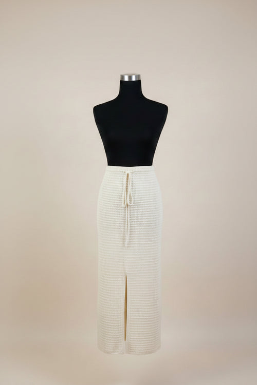 An off-white ribbed knit midi skirt with a front slit and drawstring waist, displayed on a black dress form mannequin against a solid beige background.