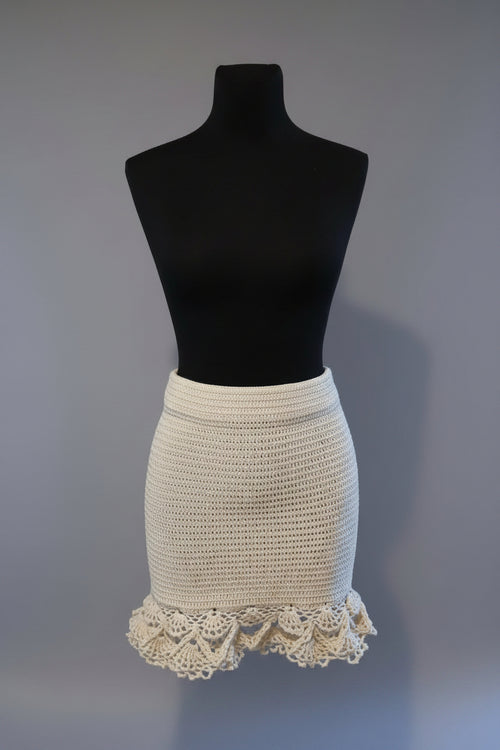 An off-white crocheted mini skirt with a scalloped lace hem, displayed on a black dress form mannequin against a neutral gray background.