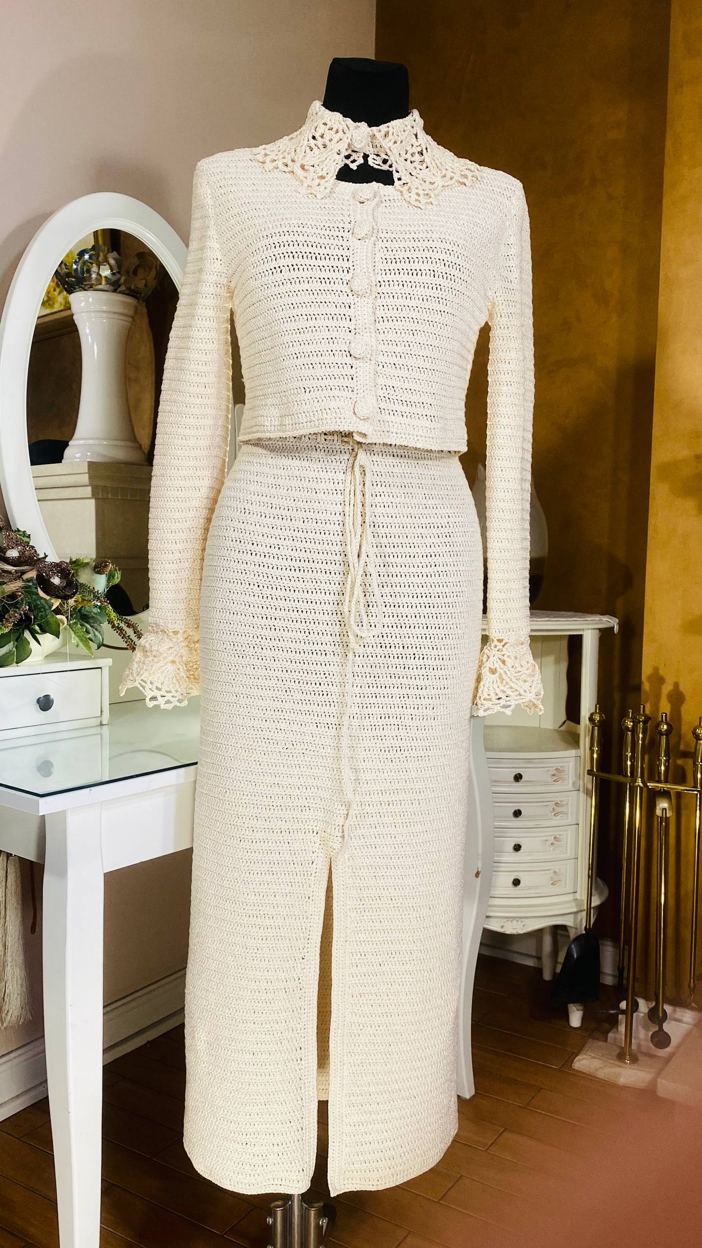 An off-white textured knit two-piece set consisting of a cropped long-sleeve jacket and a matching high-slit maxi skirt, displayed on a black mannequin in an indoor room setting.