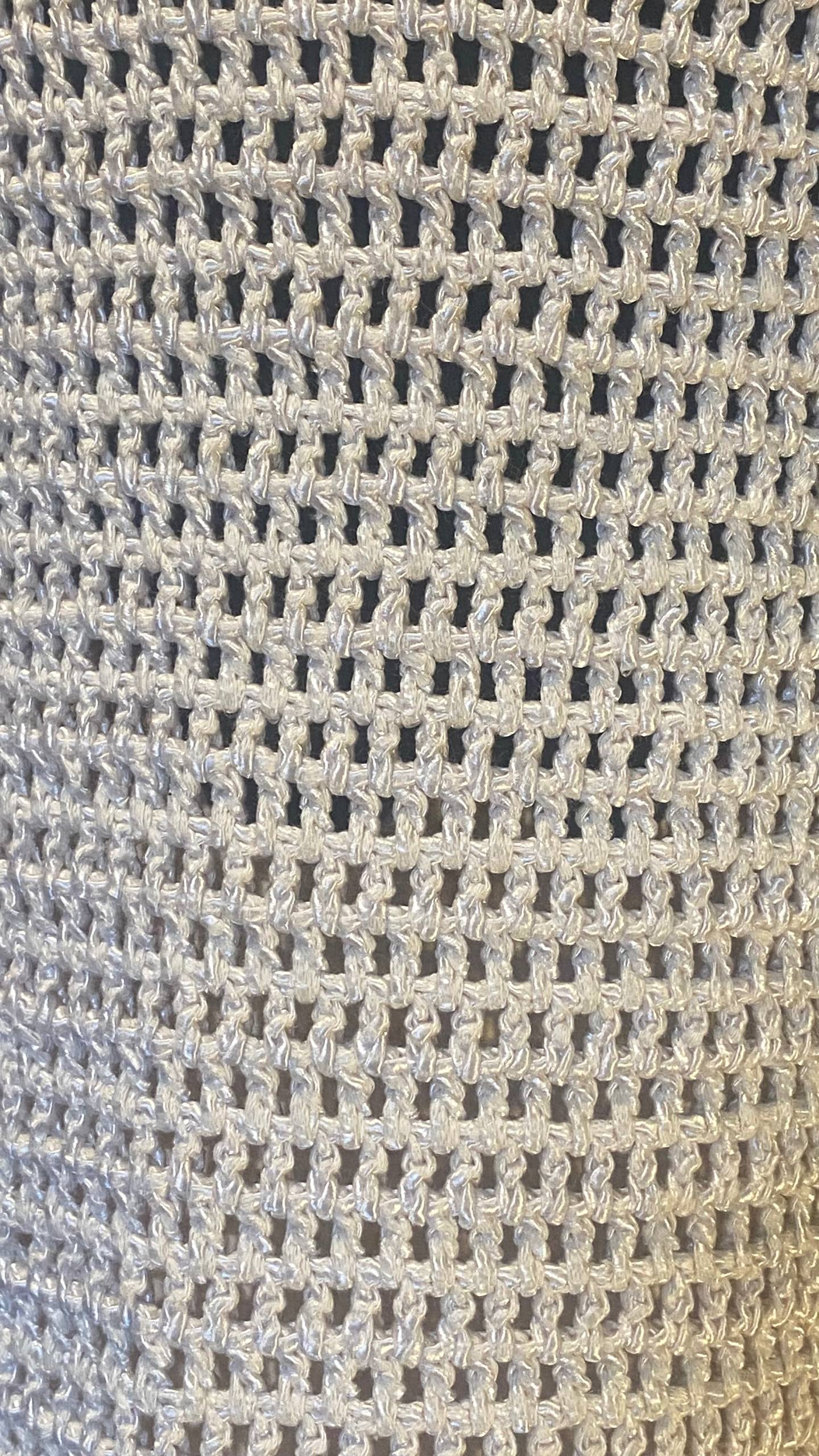 Close-up of a light gray crochet knit fabric texture with a repeating openwork pattern.